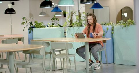African american man working on tablet sipping coffee in pastel coworking lounge