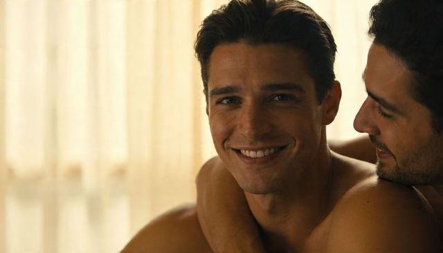 Smiling man leaning into partner in intimate embrace, warm backlit curtains, home romance