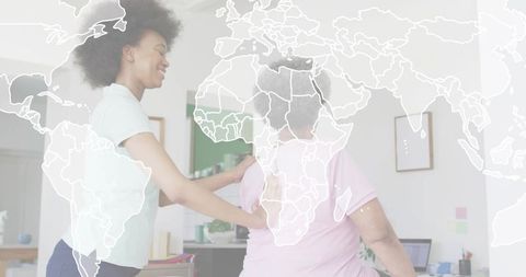 Young caregiver massaging senior woman in home office with world map overlay