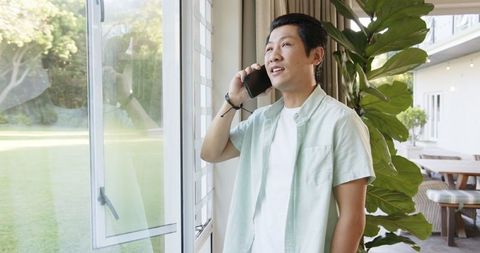 Asian Man Relaxing with Smartphone Near Window in Modern Home