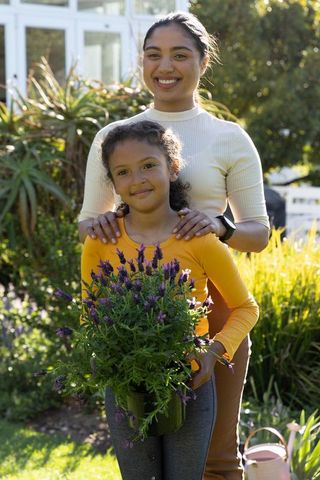 Mother and daughter gardening together in sunlit backyard holding potted lavender