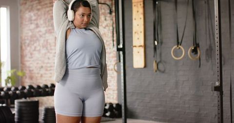 Asian woman in 20s stretching overhead in industrial gym wearing light blue activewear