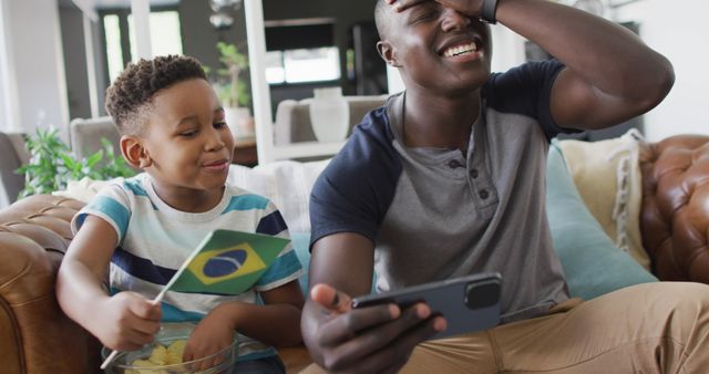 Father and son enjoying soccer match on mobile phone in living room - Download Free Stock Images Pikwizard.com