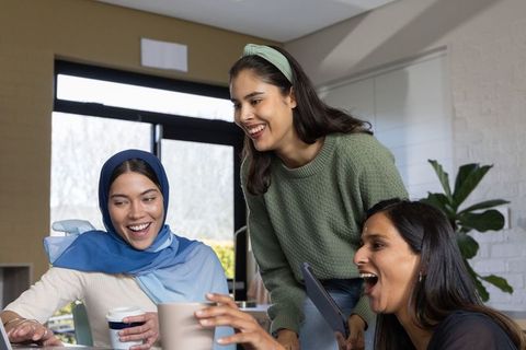 Smiling diverse women collaborating over coffee and tablet in modern cozy workspace