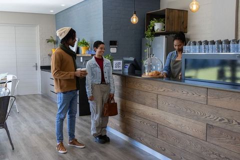 Two friends ordering coffee at wood-paneled counter with barista and pastries