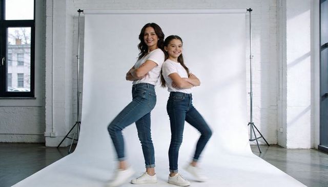 Confident mother and daughter back-to-back in white tees and jeans casual studio portrait