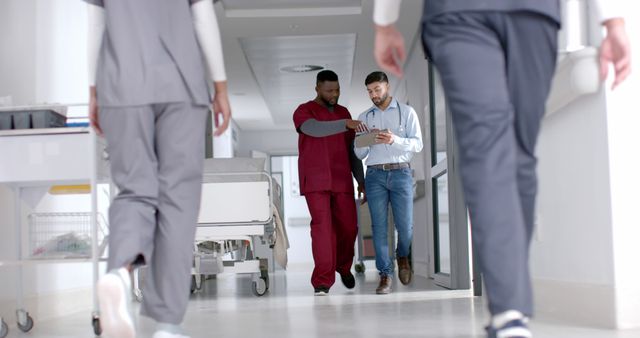 Healthcare professionals are discussing and collaborating in a modern medical facility's hallway. Medical staff in uniforms walking suggests a dynamic, fast-paced environment. Use this for articles or content related to medical teamwork, hospital routines, patient care, or modern healthcare facilities.