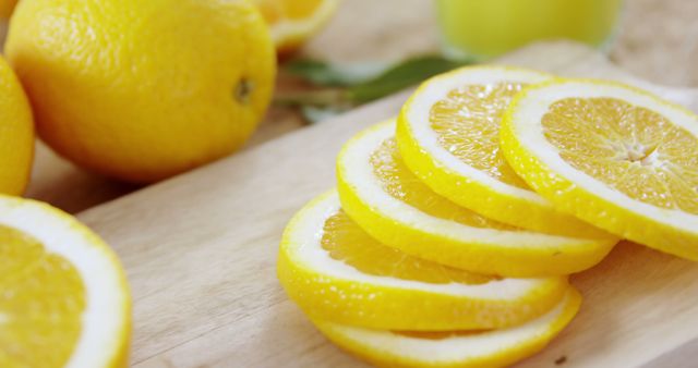 Sliced lemons are arranged on a wooden cutting board, with a whole lemon and leaves in the background, with copy space. Fresh citrus fruits like these are often used in cooking and beverages for their tangy flavor and health benefits.