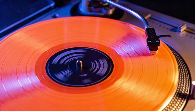 Spinning orange vinyl record on dj turntable with neon blue and purple lighting ambient glow