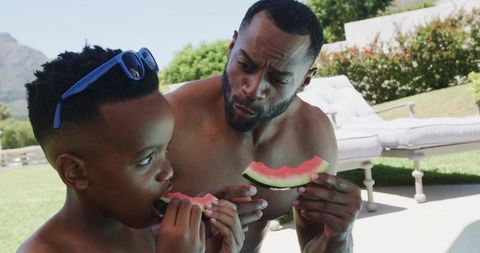African american father and teen son sharing watermelon on sunny backyard patio