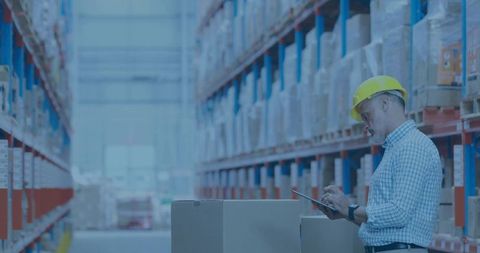 Warehouse manager inspecting inventory with tablet, wearing yellow hard hat, industrial racks