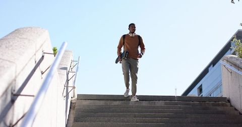 African American Man Walking Down Urban Stairs with Skateboard and Headphones