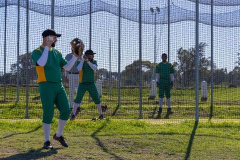 Baseball players practicing catching drill in batting cage emphasizing form and teamwork