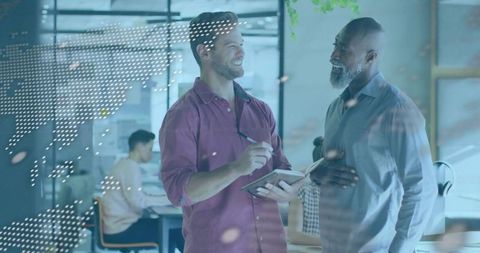 Collaborating over notebook by glass panel in modern office with digital world map overlay