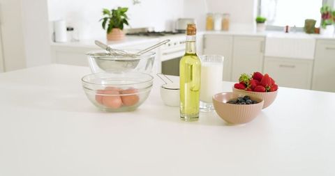 Baking ingredients with eggs, milk, and berries on white countertop