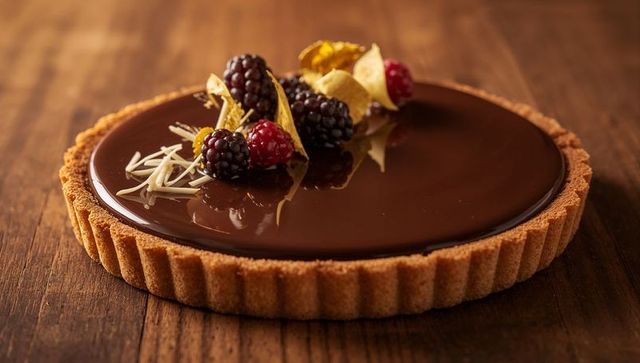 Glossy chocolate ganache tart featuring blackberries physalis and white chocolate shavings