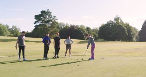 Golfers practicing putting on sunny day in green field