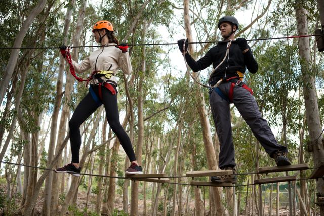 Couple holding zip line while crossing obstacle in the forest