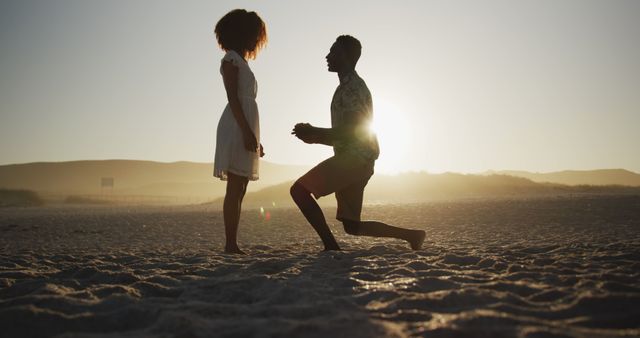This image captures a romantic moment of a beach proposal during sunset, with a couple kneeling in the sand. Ideal for use in wedding planning resources, relationship blogs, romance-themed advertisements, and engagement announcements.