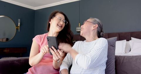 Mother and Daughter Laughing while Sharing Smartphone Moments in Bedroom