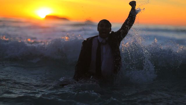 Businessman celebrating with briefcase amidst ocean waves during sunset. Represents success, determination, or resilience. Ideal for messages involving motivation, financial achievements, overcoming challenges, or work-life balance.