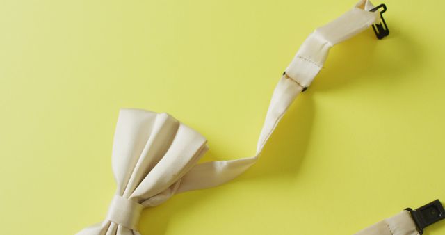 White bow tie on a bright yellow background. Ideal for promoting formal wear, menswear, and fashion accessories brands. Suitable for wedding-themed content and minimalistic design themes.