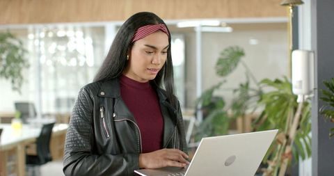 Young Professional Using Laptop in Modern Coworking Space with Indoor Plants