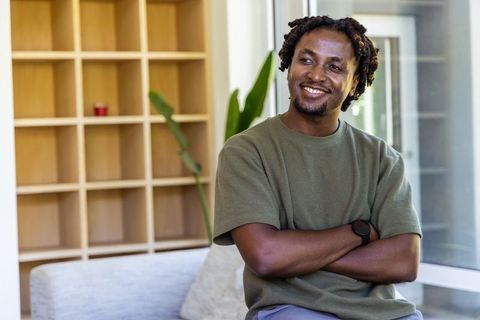 Smiling man relaxing on sofa in minimalist modern lounge with natural light and greenery
