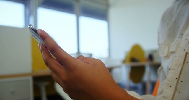 Close-up of a person holding and using a smartphone inside a modern office. Perfect for illustrating technology use, digital communication, and modern work environments.