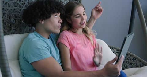 Happy couple video chatting on tablet on handsome swing chair