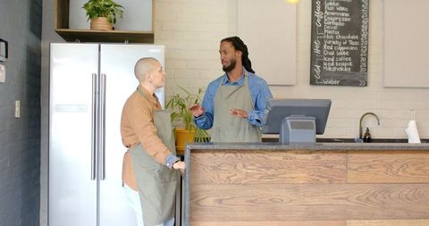 Baristas collaborating behind cafe counter discussing orders and operating register