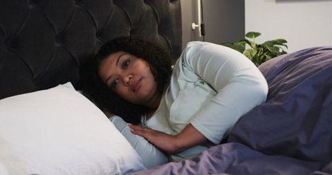 Mid Adult Woman Resting on Pillow Under Purple Duvet Relaxing in Cozy Modern Bedroom
