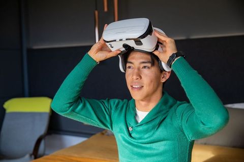Adult asian man putting on white vr headset in modern lounge wearing green sweater