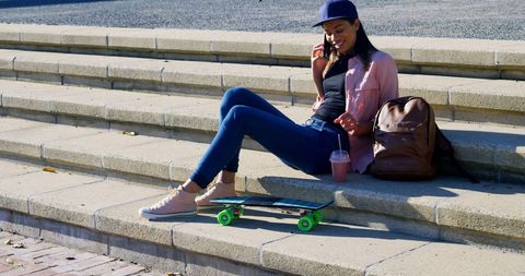 Young Woman in Urban Park Talking on Smartphone with Skateboard