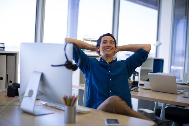 Male executive leaning back and relaxing at his desk in a modern office environment. Ideal for use in articles, advertisements, or blog posts about work-life balance, office culture, employee wellness, or corporate environments.
