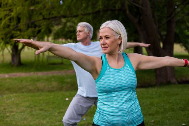 Senior couple practicing yoga in a park, focusing on balance and stretching. Ideal for promoting healthy lifestyles, fitness programs for seniors, outdoor activities, and wellness campaigns.