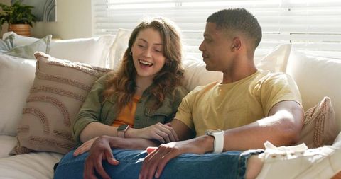 Sunlit diverse couple laughing on sofa, cozy intimate at-home moment with casual denim