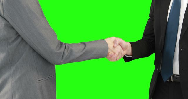 Two businessmen are engaging in a firm handshake against a green screen background, with copy space. Their professional attire suggests a formal agreement or partnership being established.