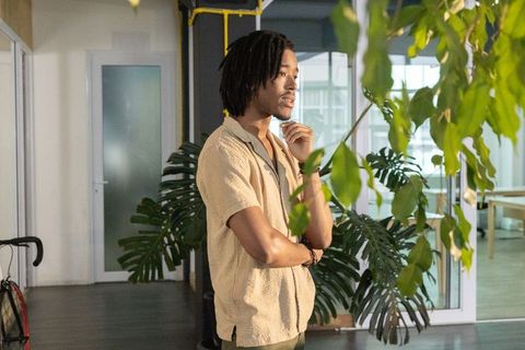African american man standing contemplative in modern glass office with lush plants