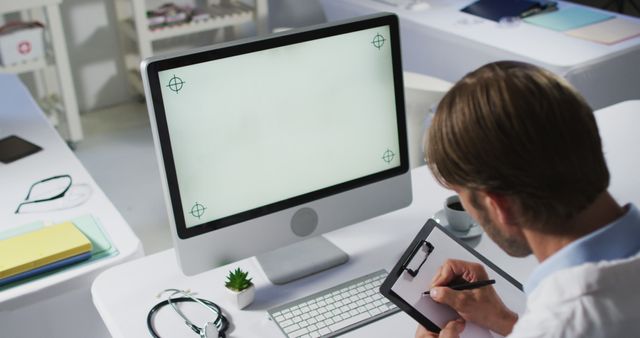 Medical professional working on digital tablet at modern office desk. Stethoscope and desktop computer visible on desk, emphasizing technology use in healthcare. Ideal for depicting modern medical practices, telemedicine, digital healthcare innovation, and professional work environments.