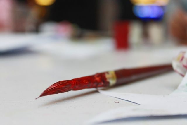 This image features a close-up view of a red paintbrush resting on a white table. It is suitable for use in educational materials, art-related blogs and websites, advertisements for art supplies, and creative project inspirations.