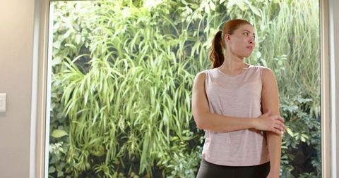 Woman stretching at home by glass door with vertical garden for workout and wellness