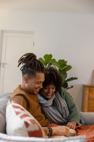 Couple cuddling on sofa examining hands while wearing knit sweaters and scarf