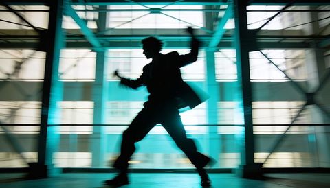 Silhouette dancer striking wide pose in glass atrium with motion blur and teal light
