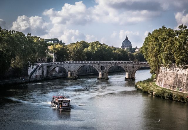 Tourist boat travels along Tiber River beneath ancient stone bridge with Vatican City's St. Peter's Basilica visible in background. Rome's historic architecture and natural scenery combine for an iconic European travel experience. Ideal for travel blogs, tourism companies, cultural and historical features.