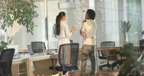 Diverse team brainstorming at glass whiteboard in modern open-plan office