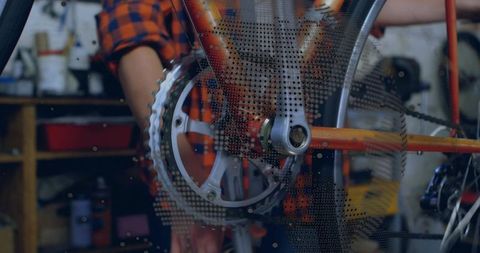 Mechanic adjusting bicycle crankset and chainring in workshop wearing orange plaid shirt