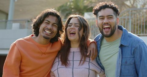 Laughing friends embracing on sunny terrace, diverse young adults sharing candid joy