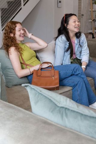 Diverse friends laughing and chatting on beige sectional sofa with handbags casual home