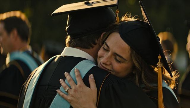 Graduates embracing on campus at golden hour wearing mortarboards and light-blue hoods